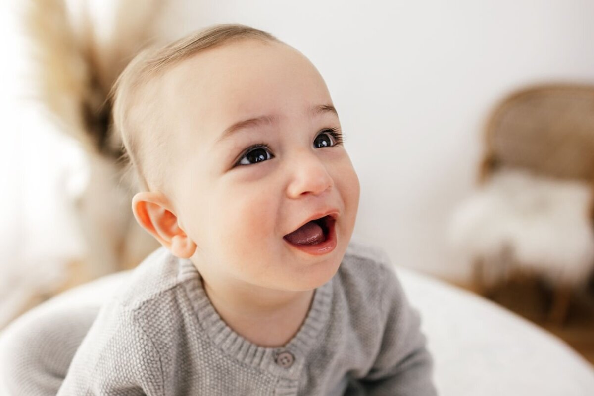 Close-up portrait of a happy baby with bright eyes and an open mouth, looking upwards with a joyful expression in a bright setting in UK