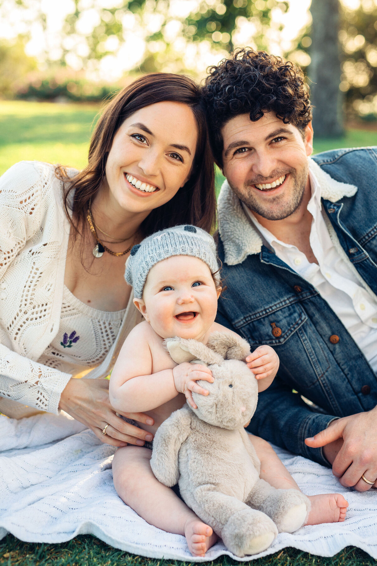 Family Portrait Photo Of Couple Smiling With Their Baby While Seated On The Ground In Los Angeles