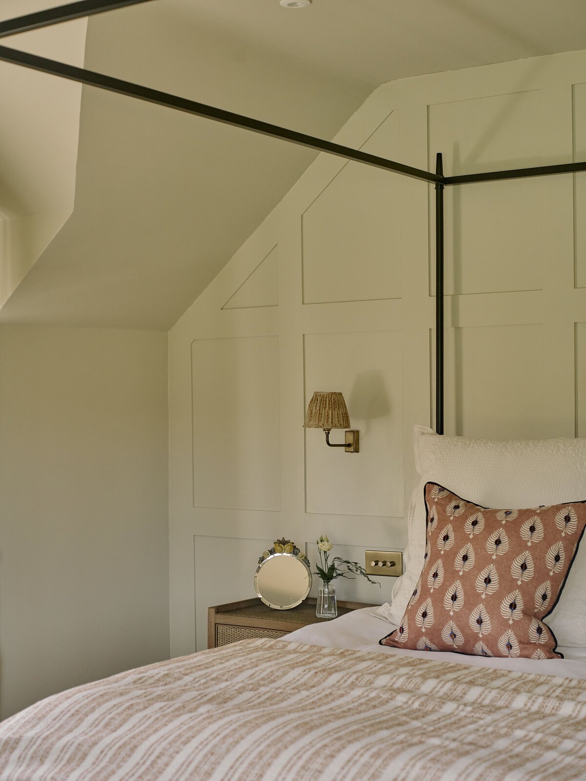 Four posted bed with side table and small mirror in front of panelled walls