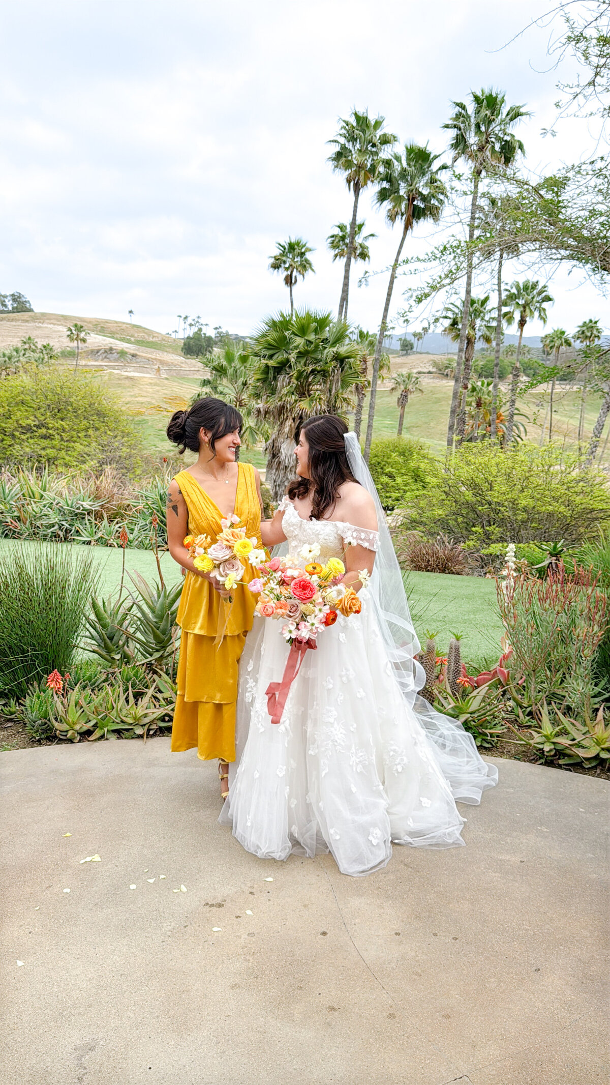 Bride and her maid of honor and matron of honor smiling during their portraits holding colorful bouquets on her wedding day at the San Diego Zoo Safari Park.