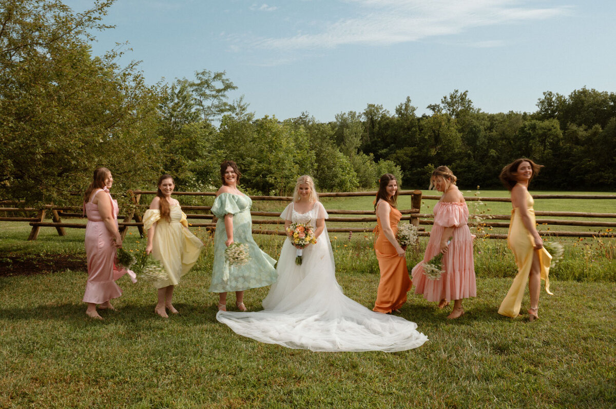 Bride with bridesmaids in pastel dresses walking in a field