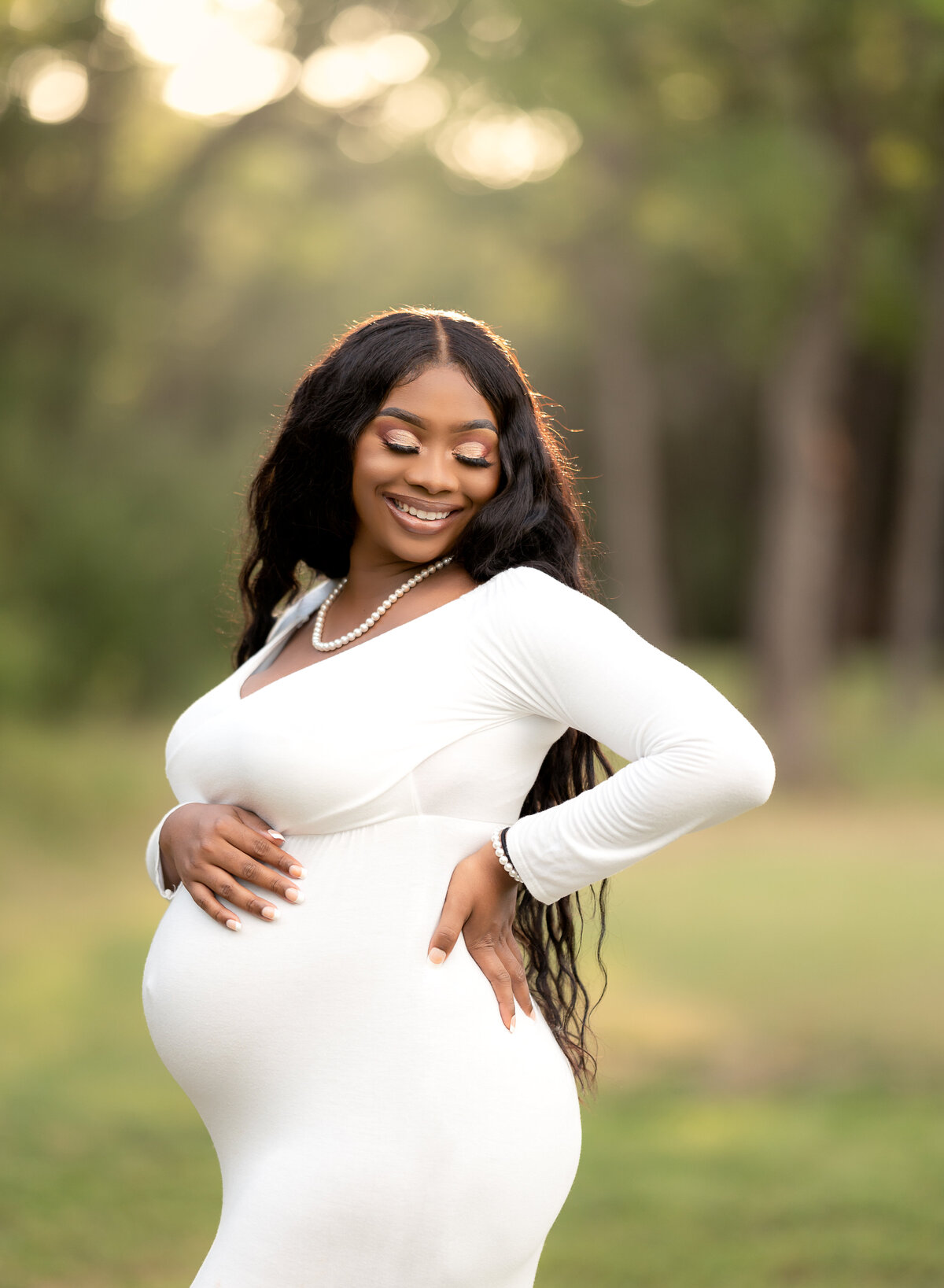 woman smiling while posing holding her pregnant belly in a white fitted dress
