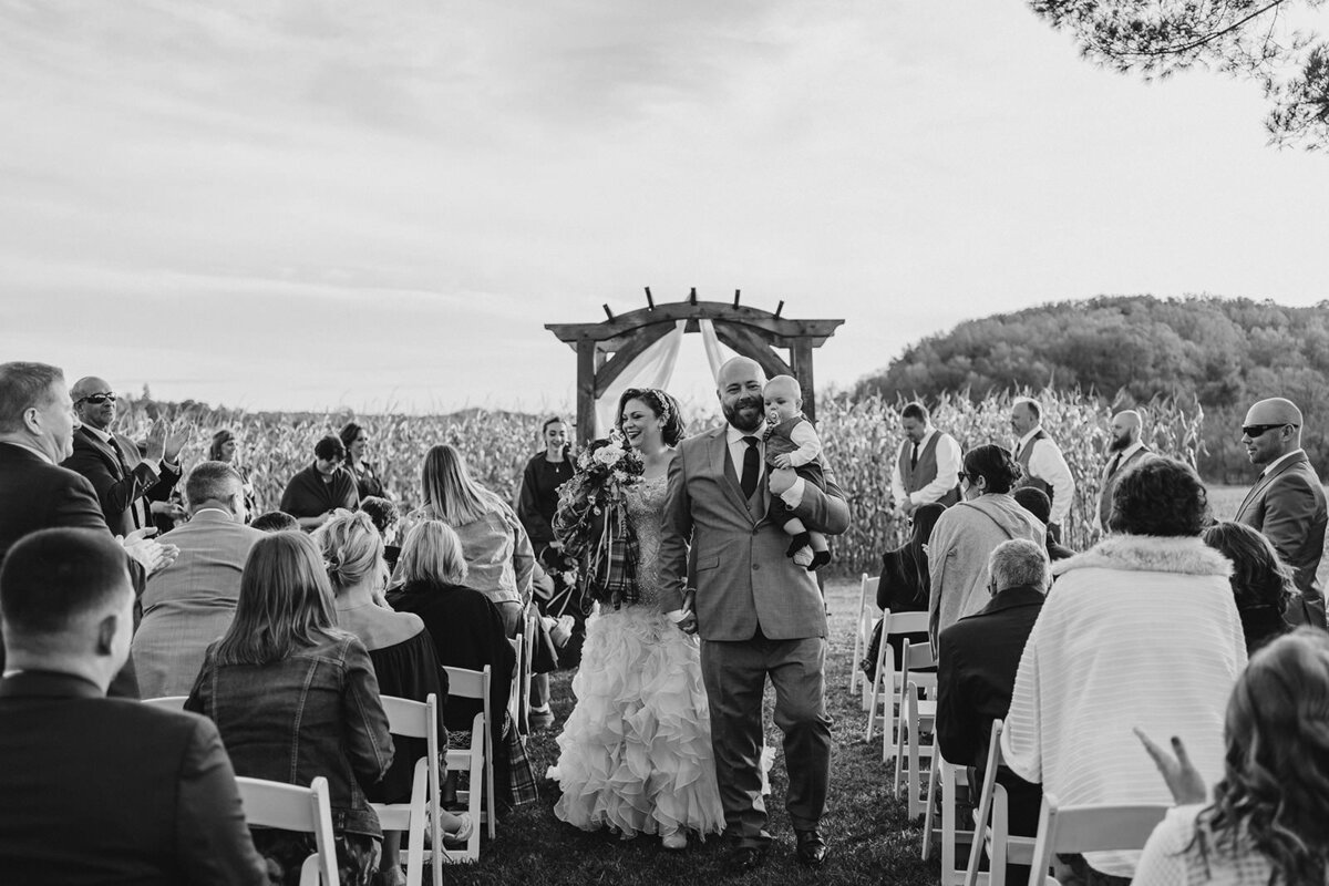 Newlyweds walking back up the aisle together as one holds a baby 