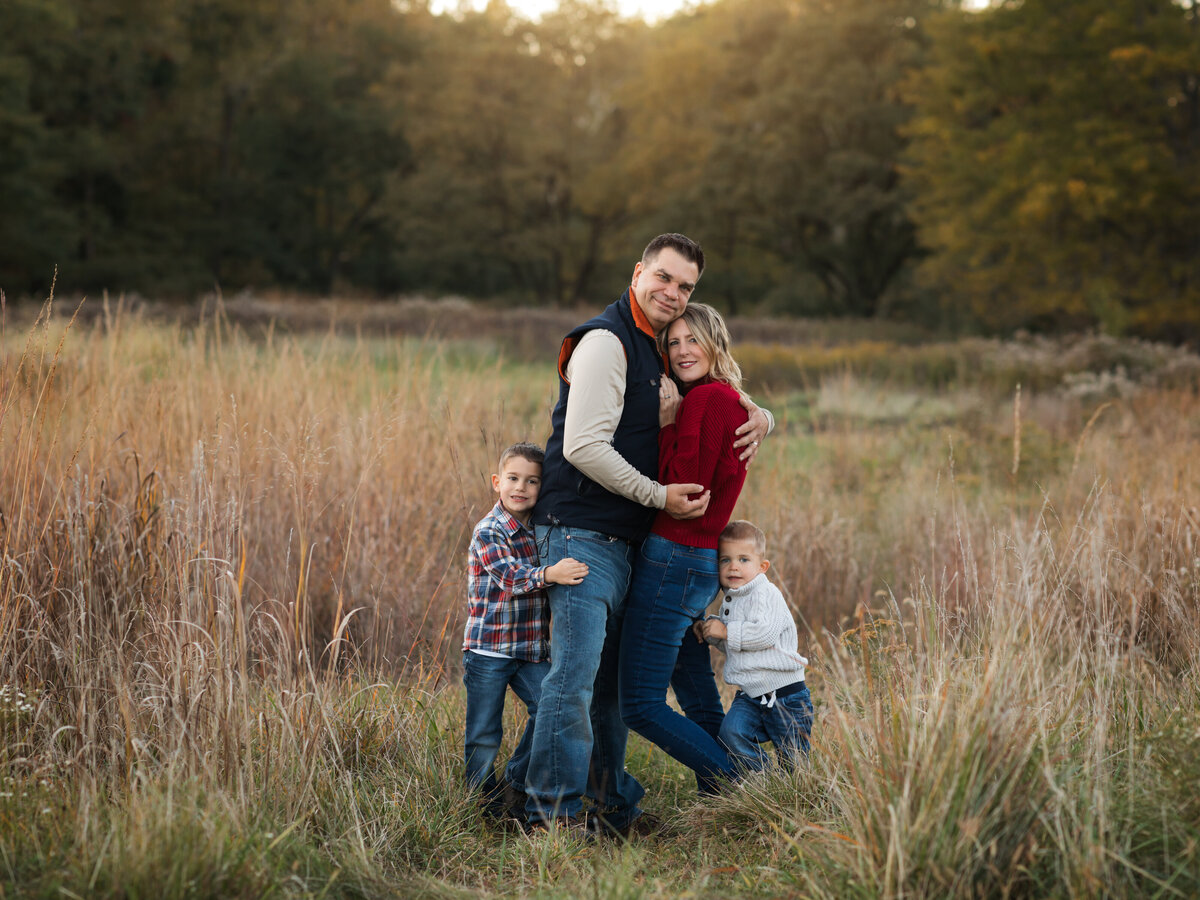 mom dad and two sons posed in field for family photoshoot 