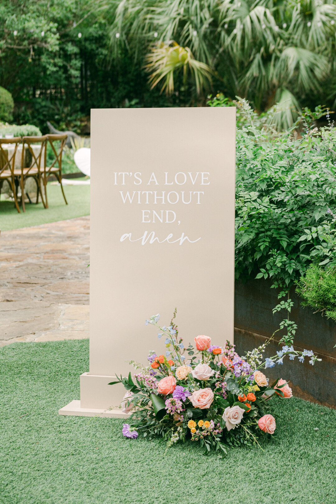 Wedding welcome sign reading “It’s a love without end amen” surrounded by pastel spring floral bouquet at an outdoor garden ceremony in Texas Hill Country, photographed by Marina Lazarine Photography.