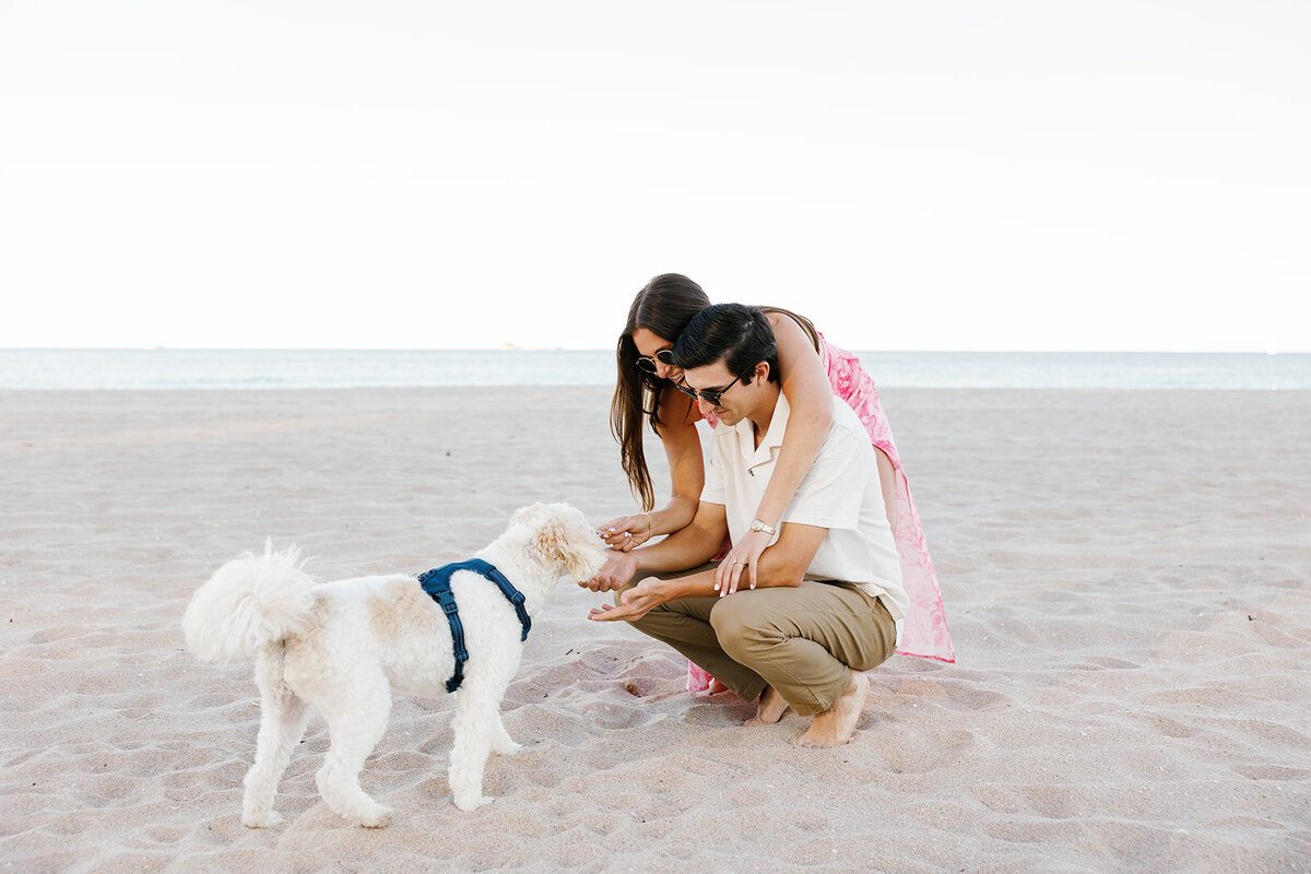 Rebecca and Graysen share a playful moment with their dog on the beach, incorporating their furry companion into their romantic engagement session at Marriott Hotel Fort Lauderdale.