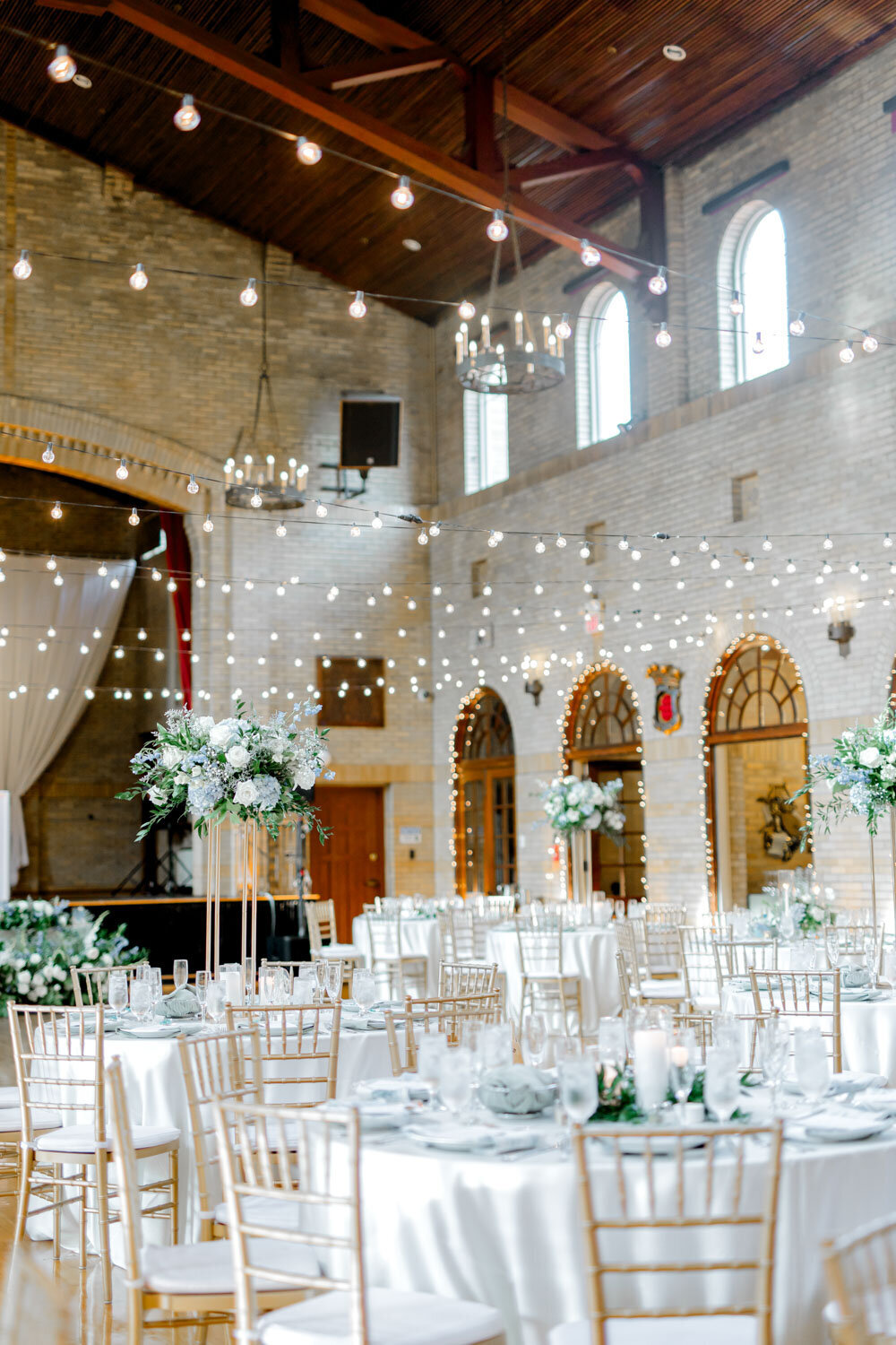 Wide view of reception hall with string lights and tall centerpieces