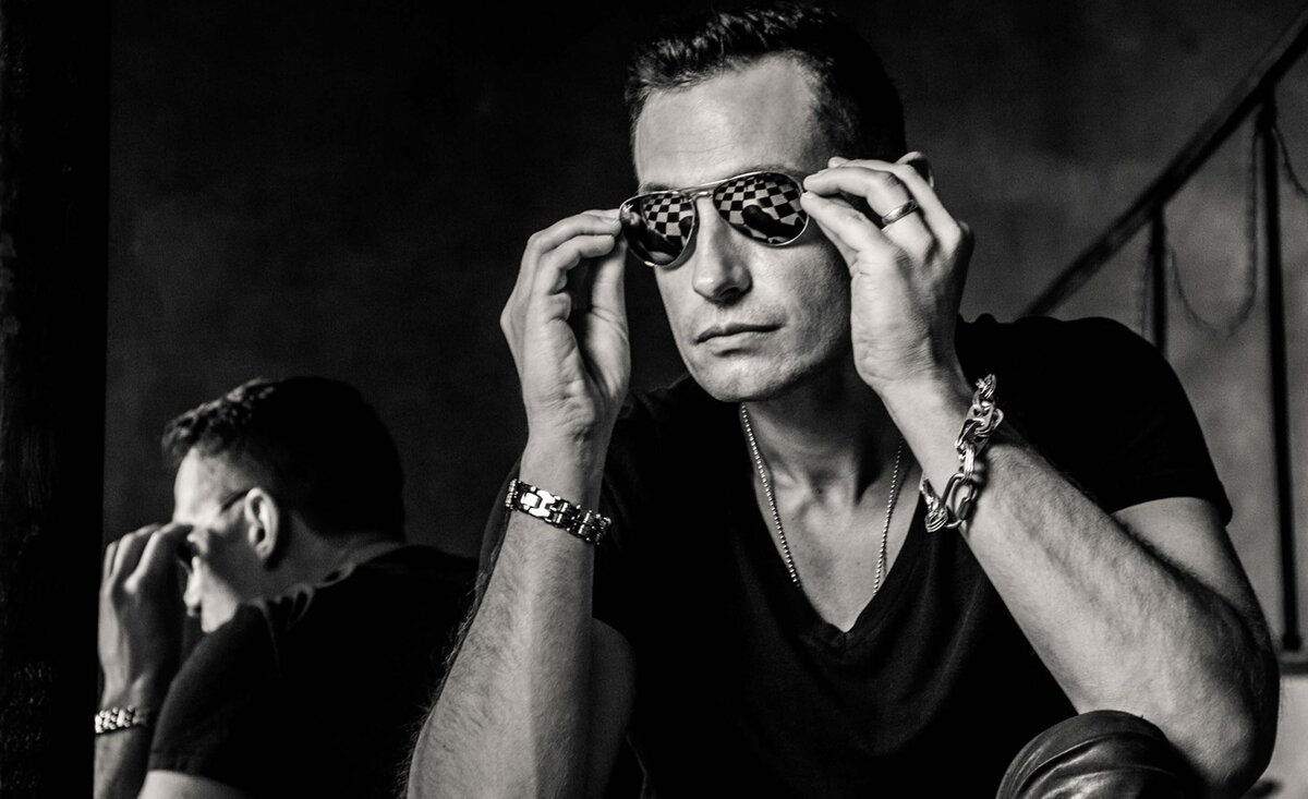 Male musician portrait Adam Rutledge black and white sitting holding sunglass arms with checkered floor reflections in  lenses