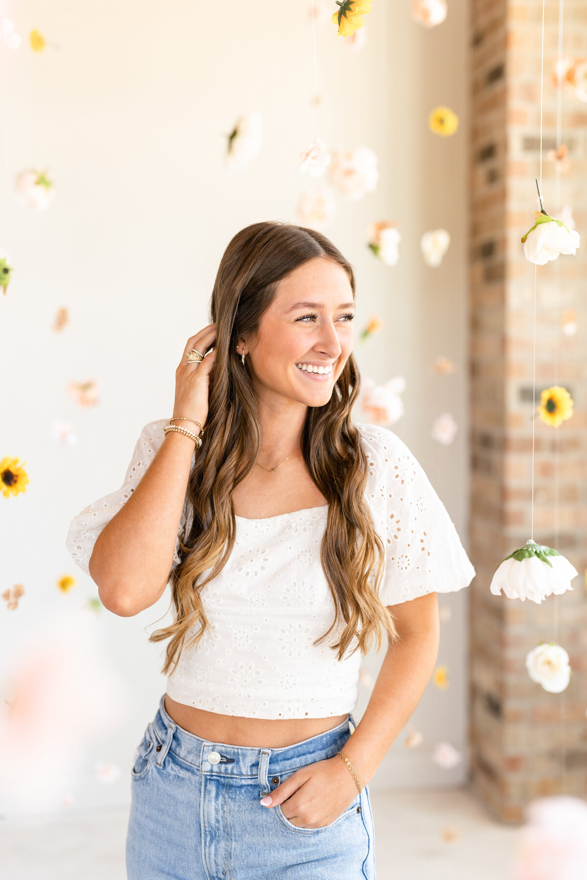 Texas A&M senior girl standing with hand in pocket and other hand in hair and laughing away in the middle of a hanging garden at Bravely Studio