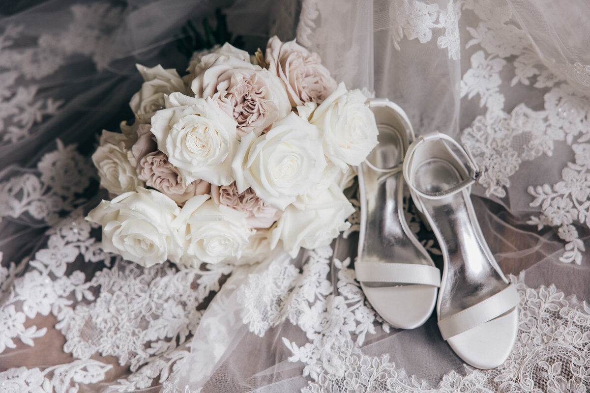 Detail shot of white bridal heels with luxurious bouquet of white and pink roses