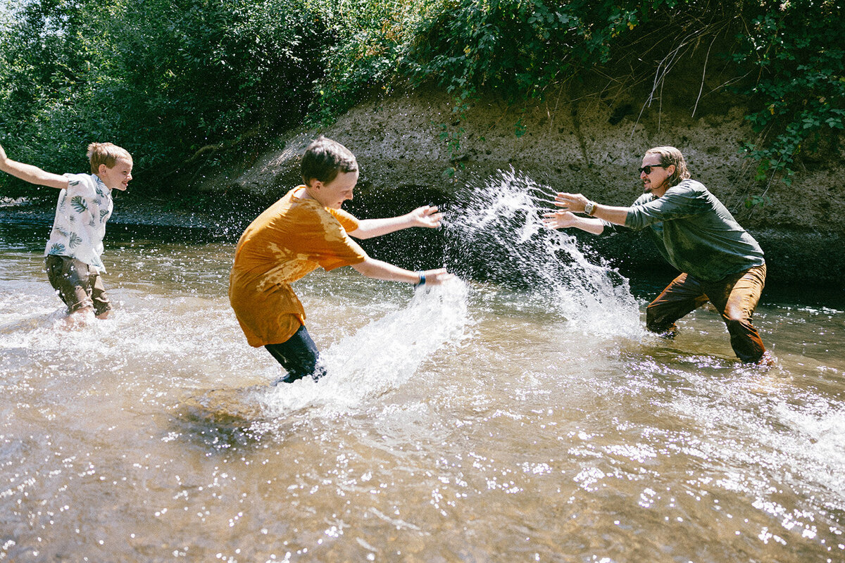 Family splashes and plays together in candid moments during a photo session. 