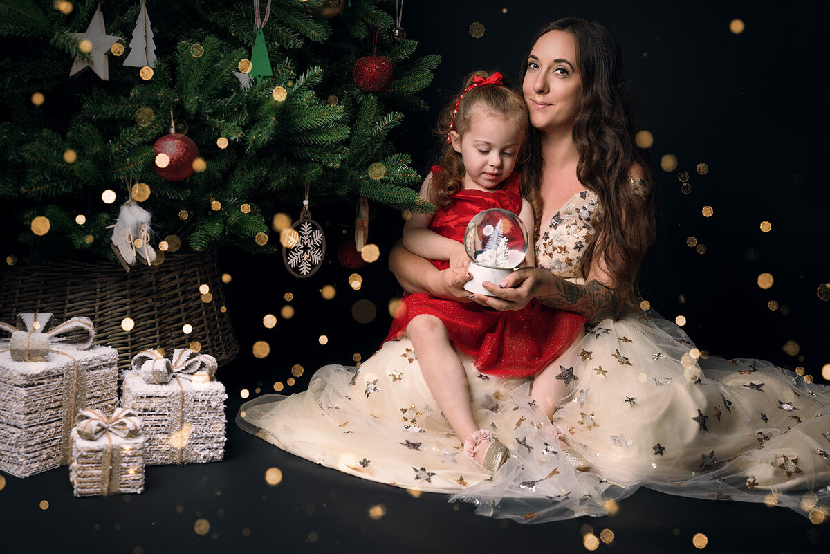 Image of a Mum & Daughter cradling a snow globe on a Christmas backdrop in the studio. Taken by Norwich portrait photographer Claire Howes. Christmas Mini Sessions Norwich.