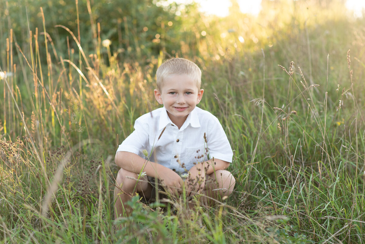 Boy squatting in a field at sunset, smiling at the camera
