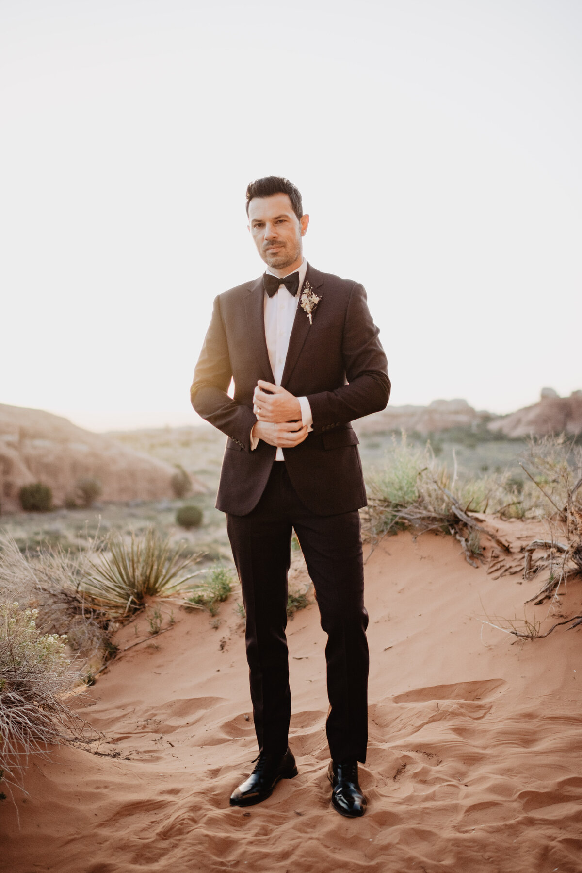 Utah elopement photographer captures groom adjusting sleeves on Arches National Park wedding