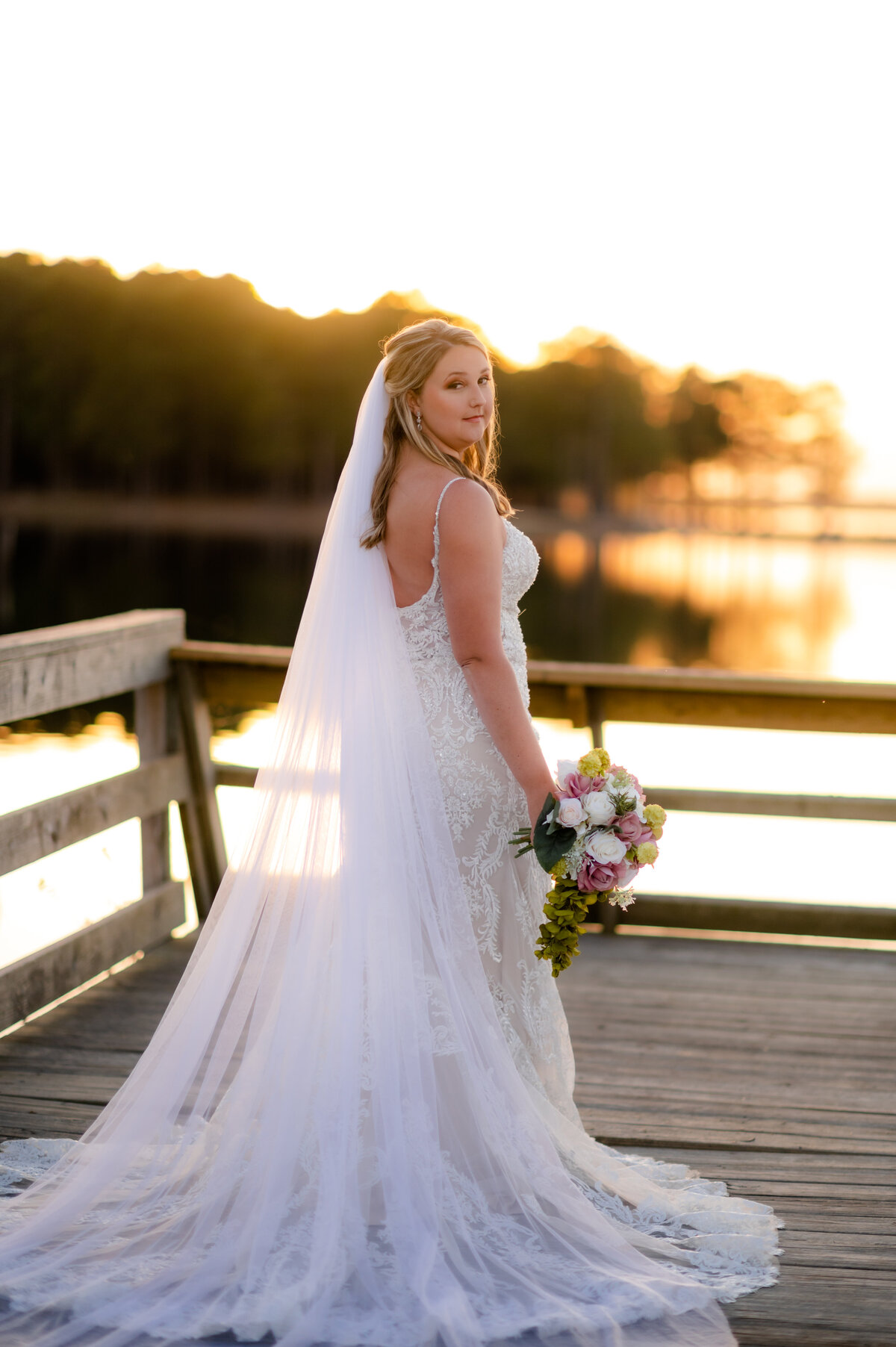 outdoor bridal session with bride at the end of a dock looking back over her shoulder to the camera while the sun sets behind her