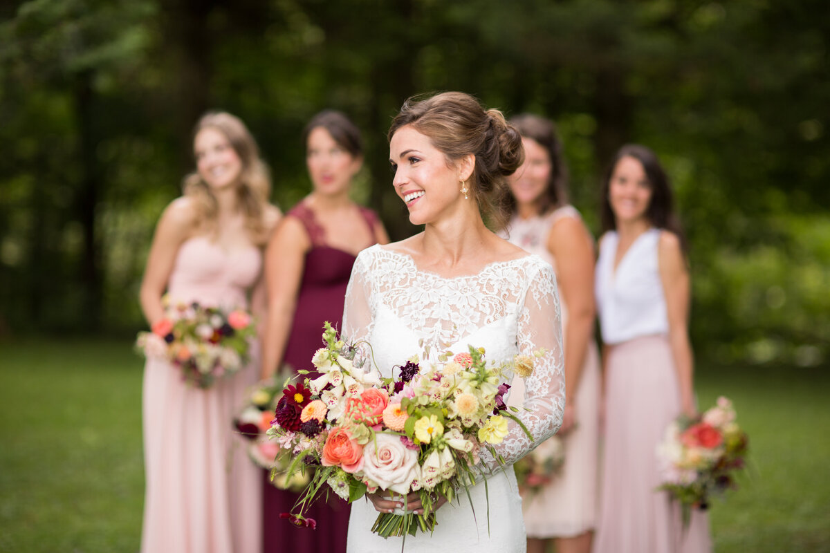 A smiling bride holds a bouquet in a Montreal garden, with her bridesmaids behind her.