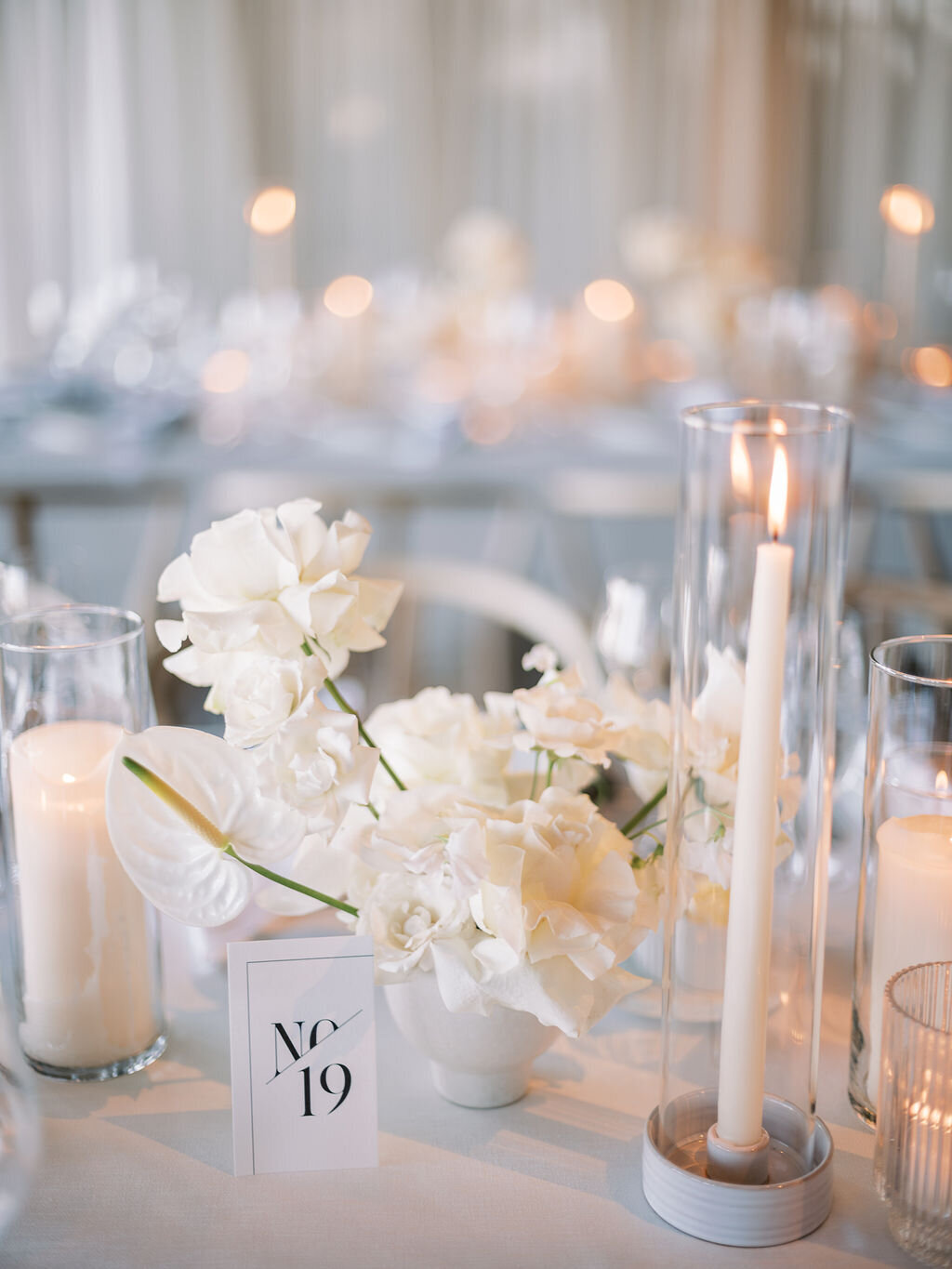 A detailed view of a wedding table with delicate white flowers and tall glass-encased candles.