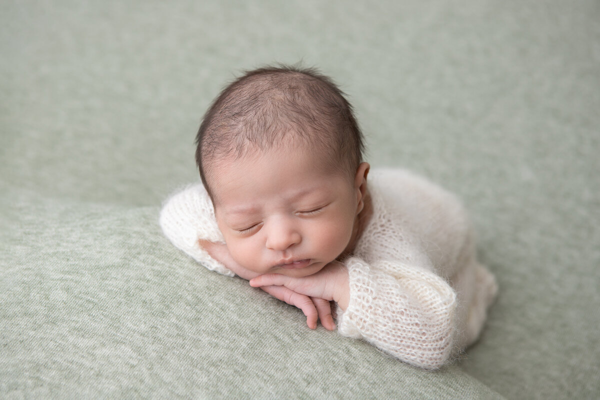 Chin on hands studio table posed newborn on a pastel green backdrop