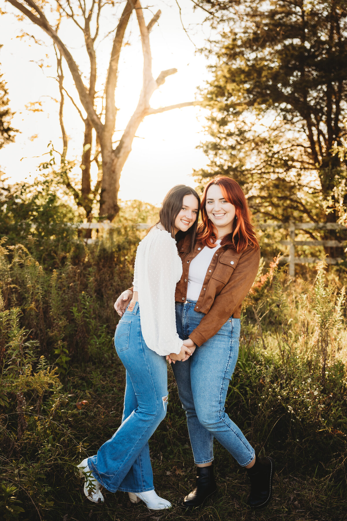 A redheaded and a brunette woman embrace in front of trees
