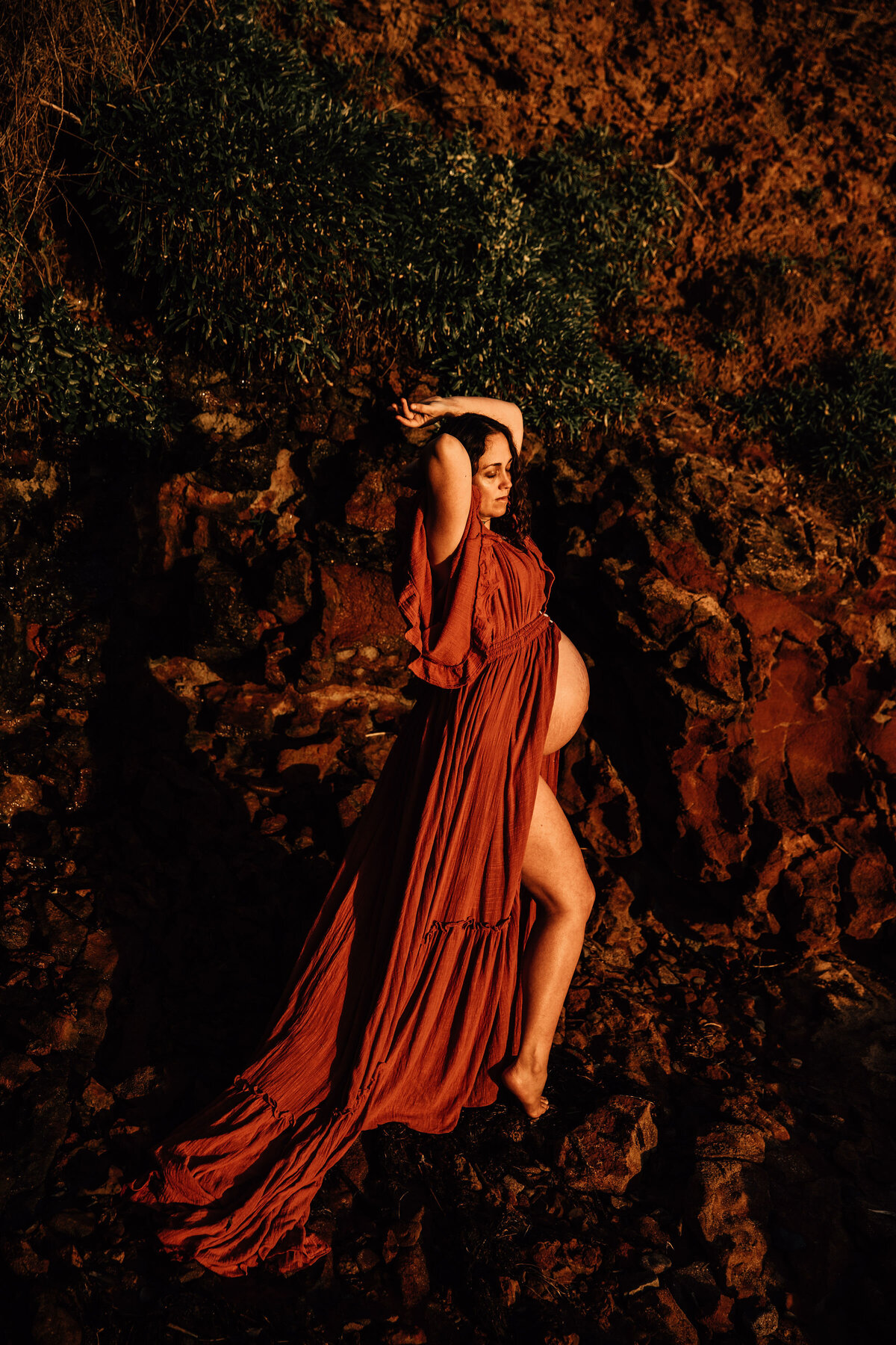Pregnant woman in red gown stands against red rocks