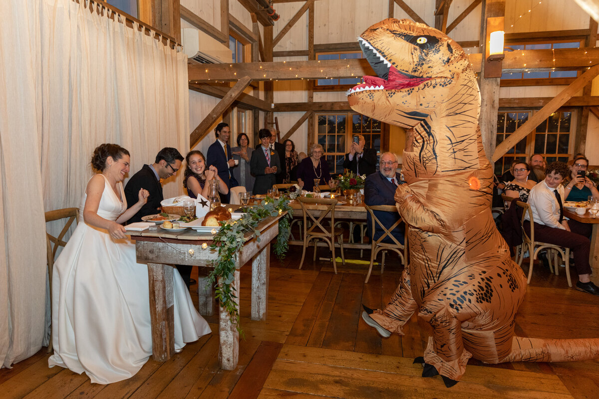 A dinosaur dancing in front of a bride and groom at a reception.