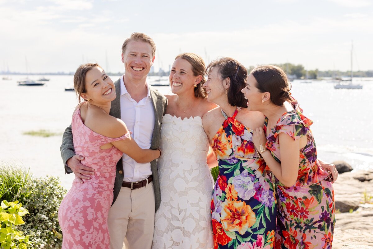 groom and bride hugging family during portraits by the water at American Yacht Club in Rye, NY