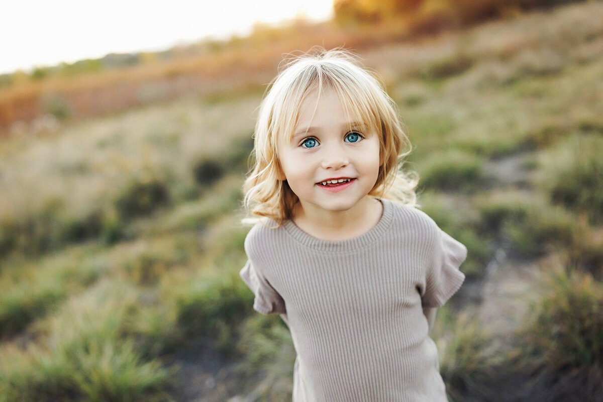 Toddler girl grins at the camera for family pictures in Fort Collins