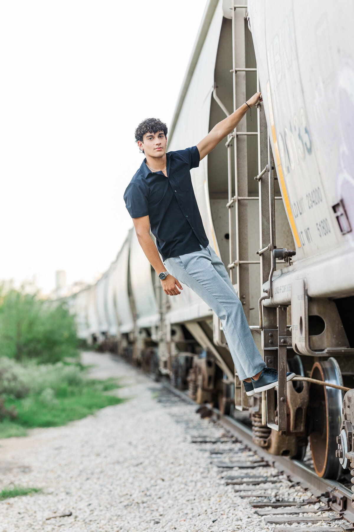 A creative and dynamic senior photo of a young man climbing a train car in Mule Alley, Fort Worth. This portrait blends personality and grit with artistic style, photographed by Jennifer Lynn Photography.
