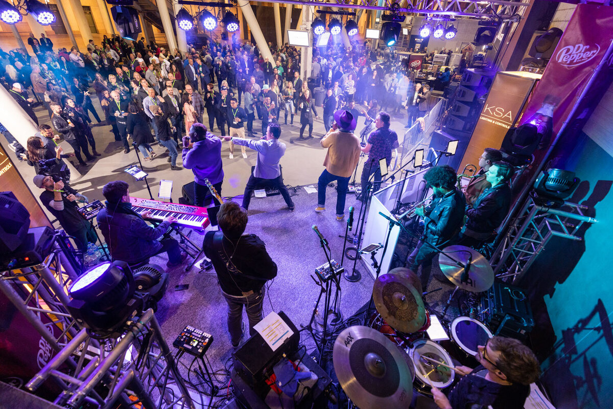 Band playing on stage with purple lighting and large crowd.