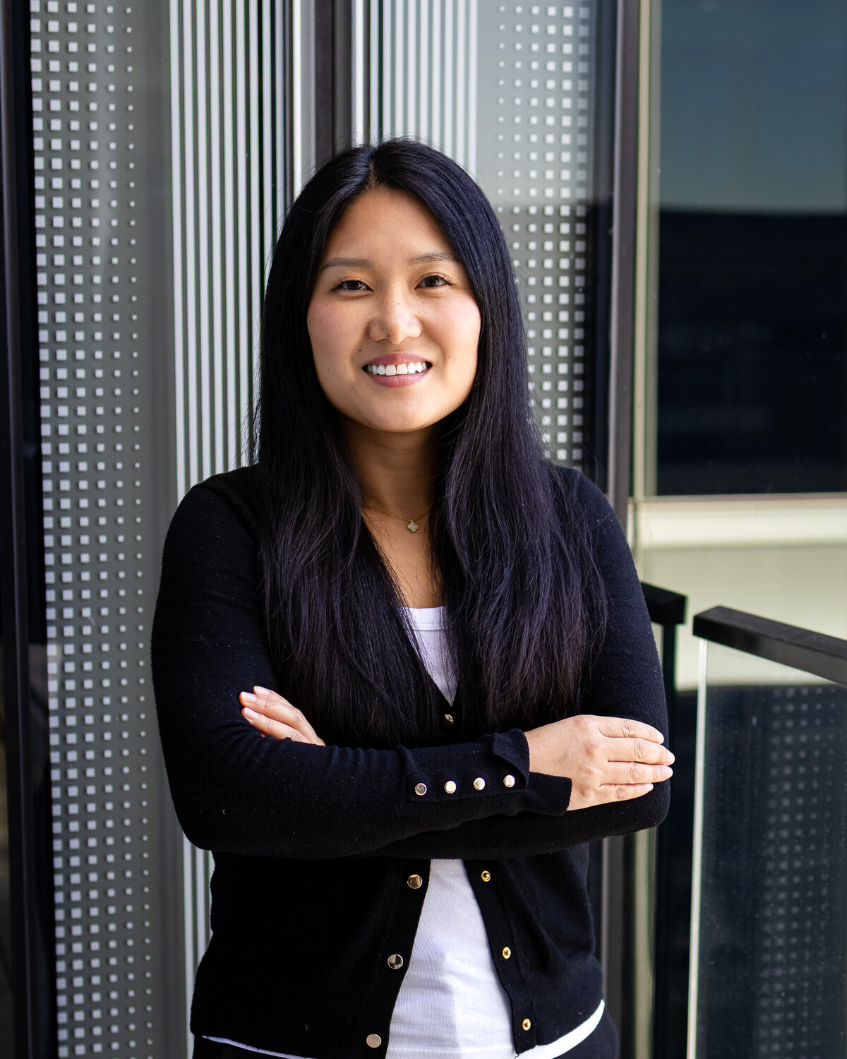 Woman in black cardigan smiling by office building window – Bay Area Headshot Portfolio – Ellobelle Photography