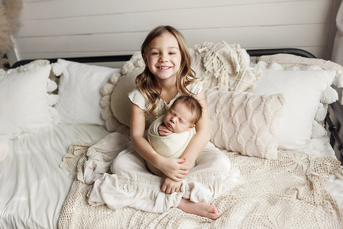 Bis sister lovingly holding baby brother who's all wrapped up.