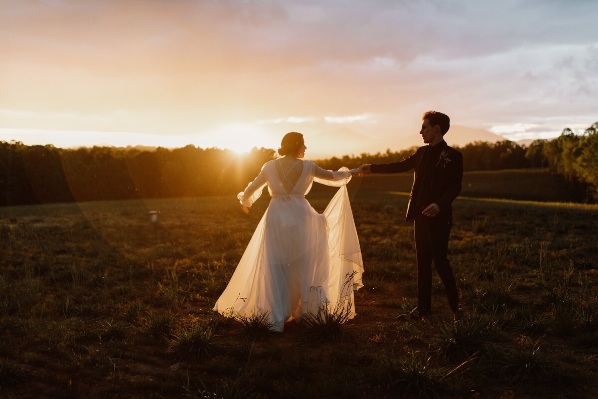 bride and groom interlocking hands in grass field
