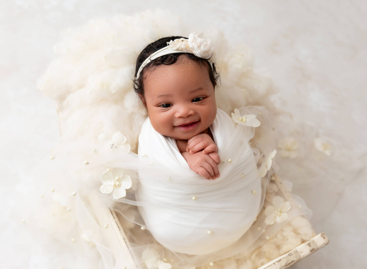 Newborn baby girl smiling wrapped in pearls wrap with flowers