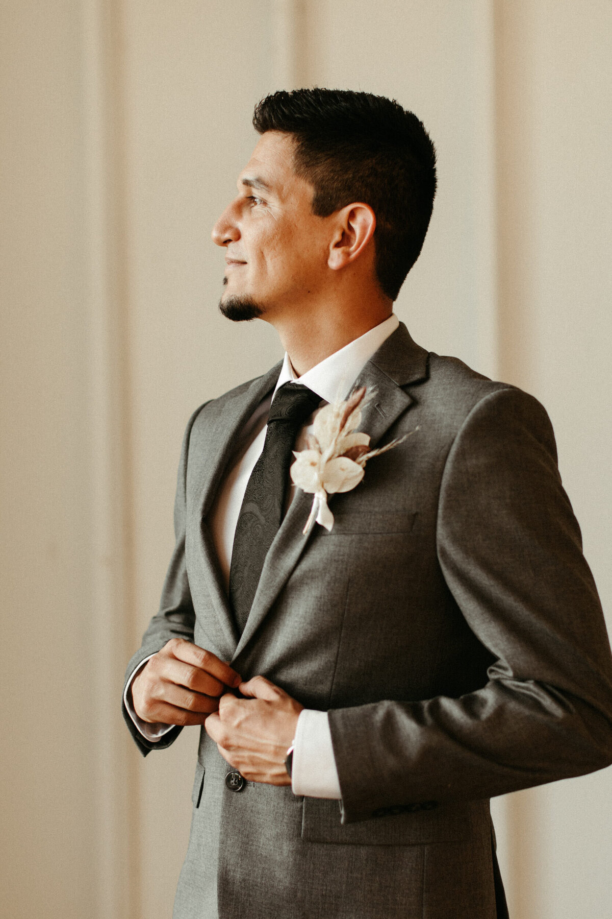 Groom buttoning his grey suit and looking out the window