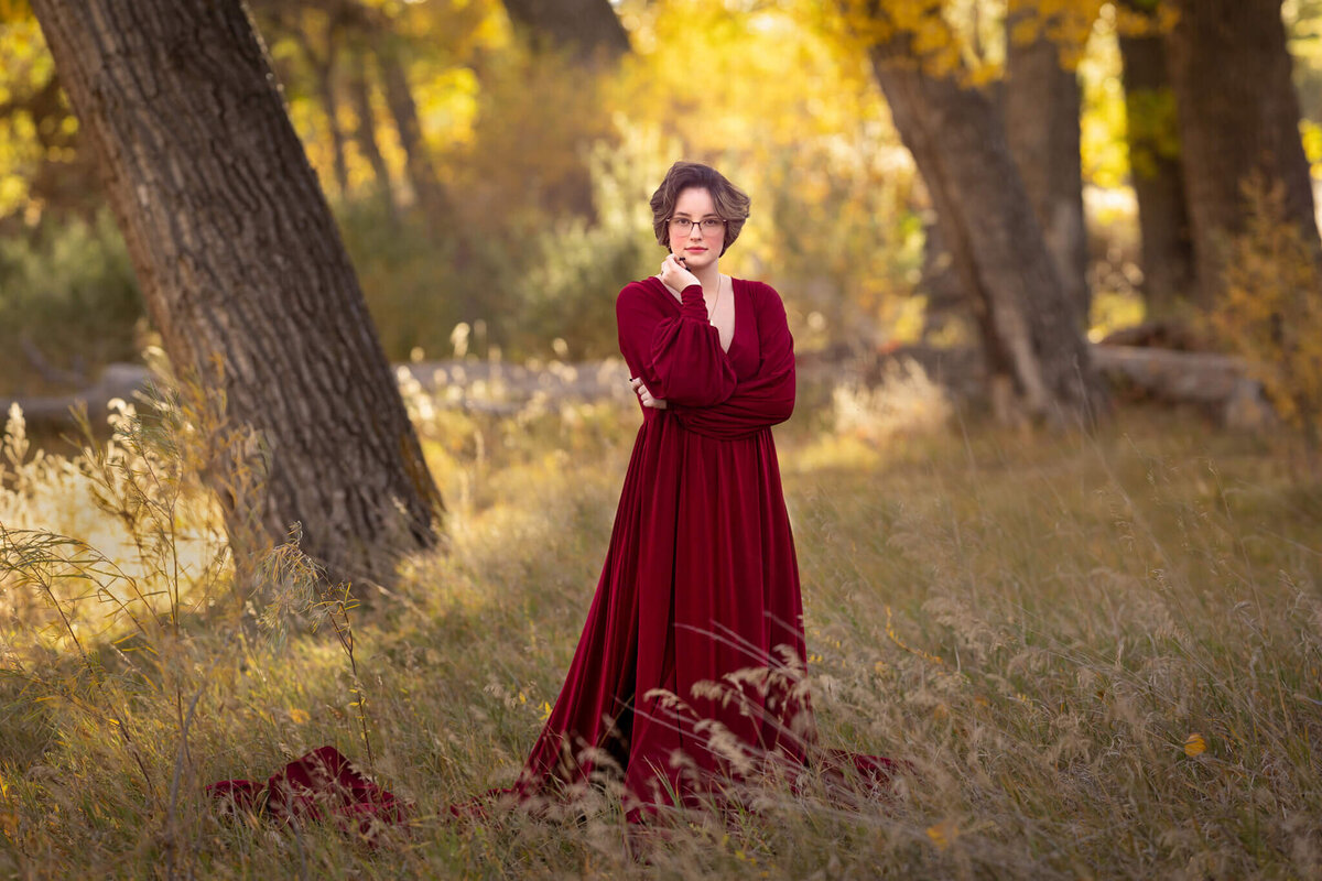teenage girl wearing a flowy red dress standing in a field