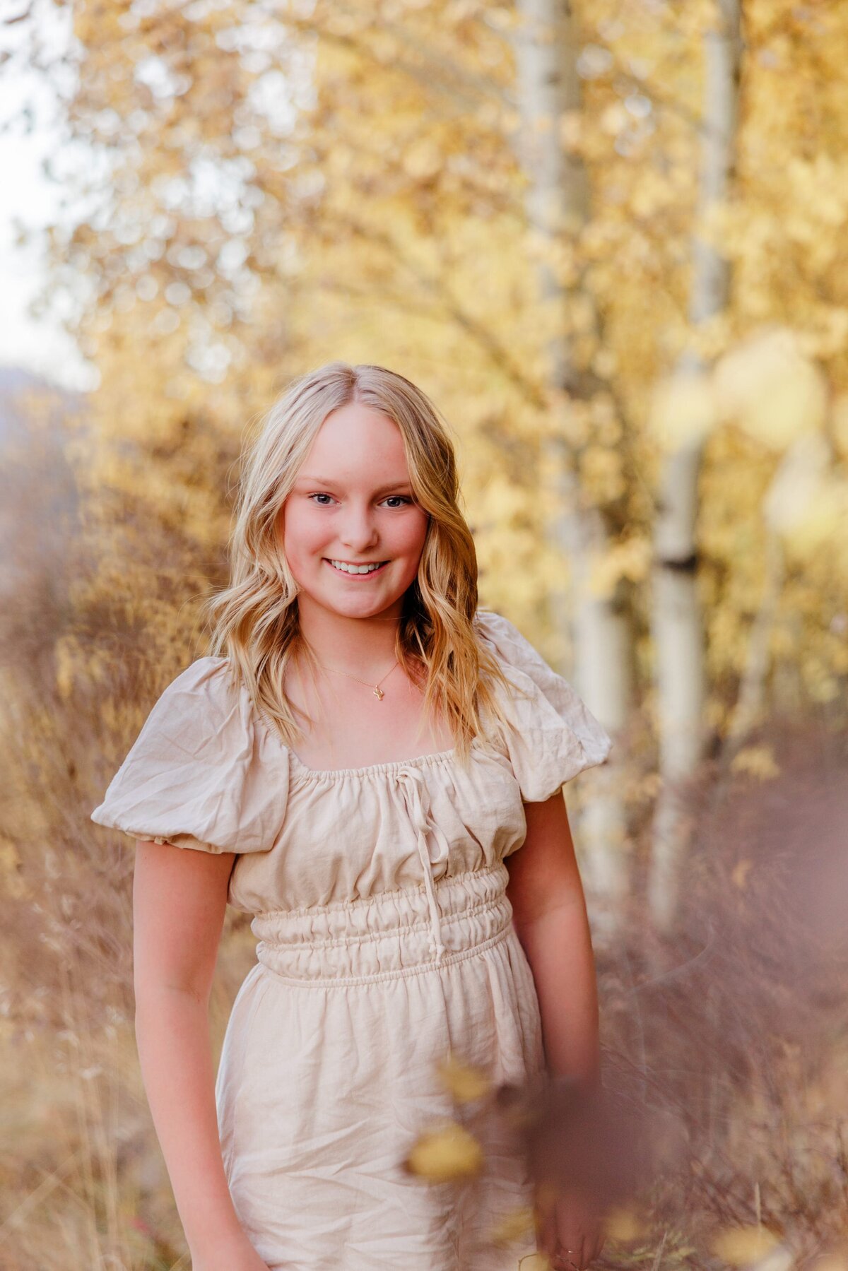 A happy teenage girl smiles in a cream dress in a fall forest