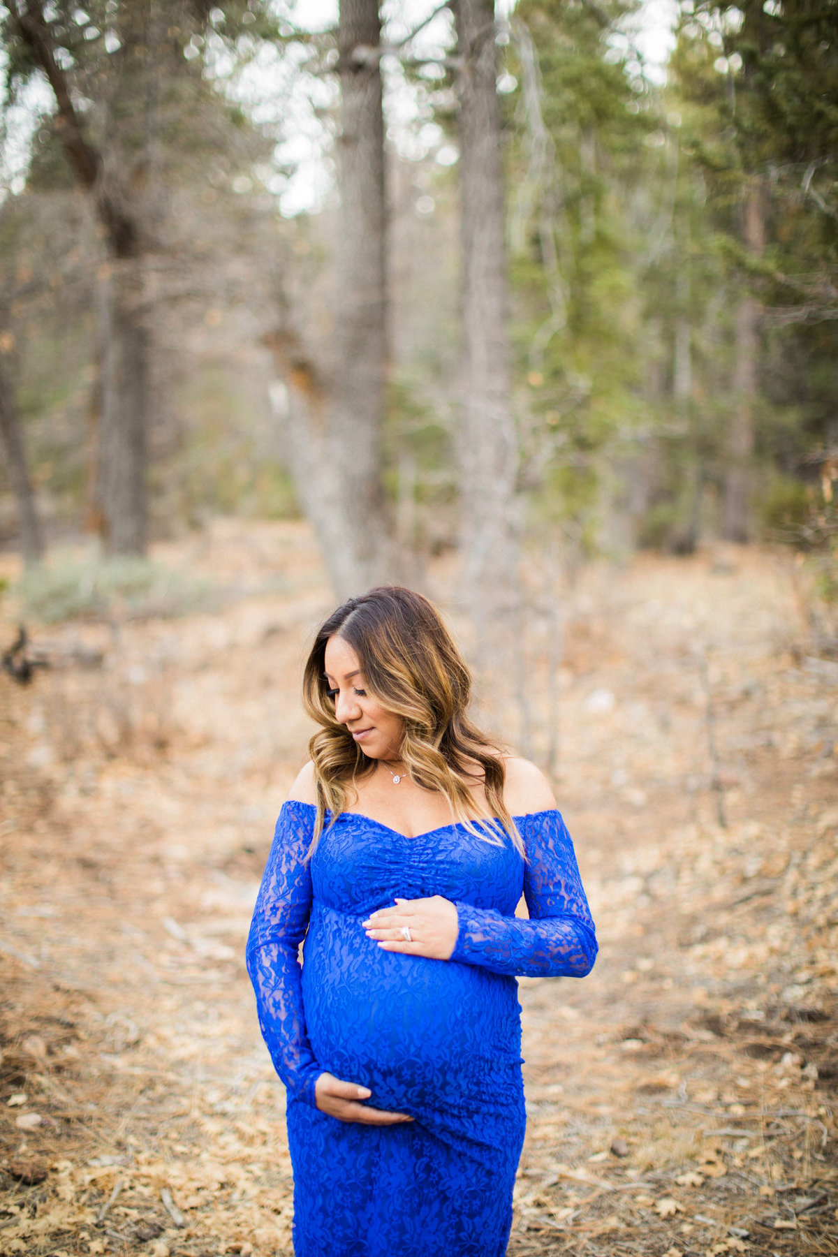 Mother to be poses while holding her belly during a maternity photo session in the mountains