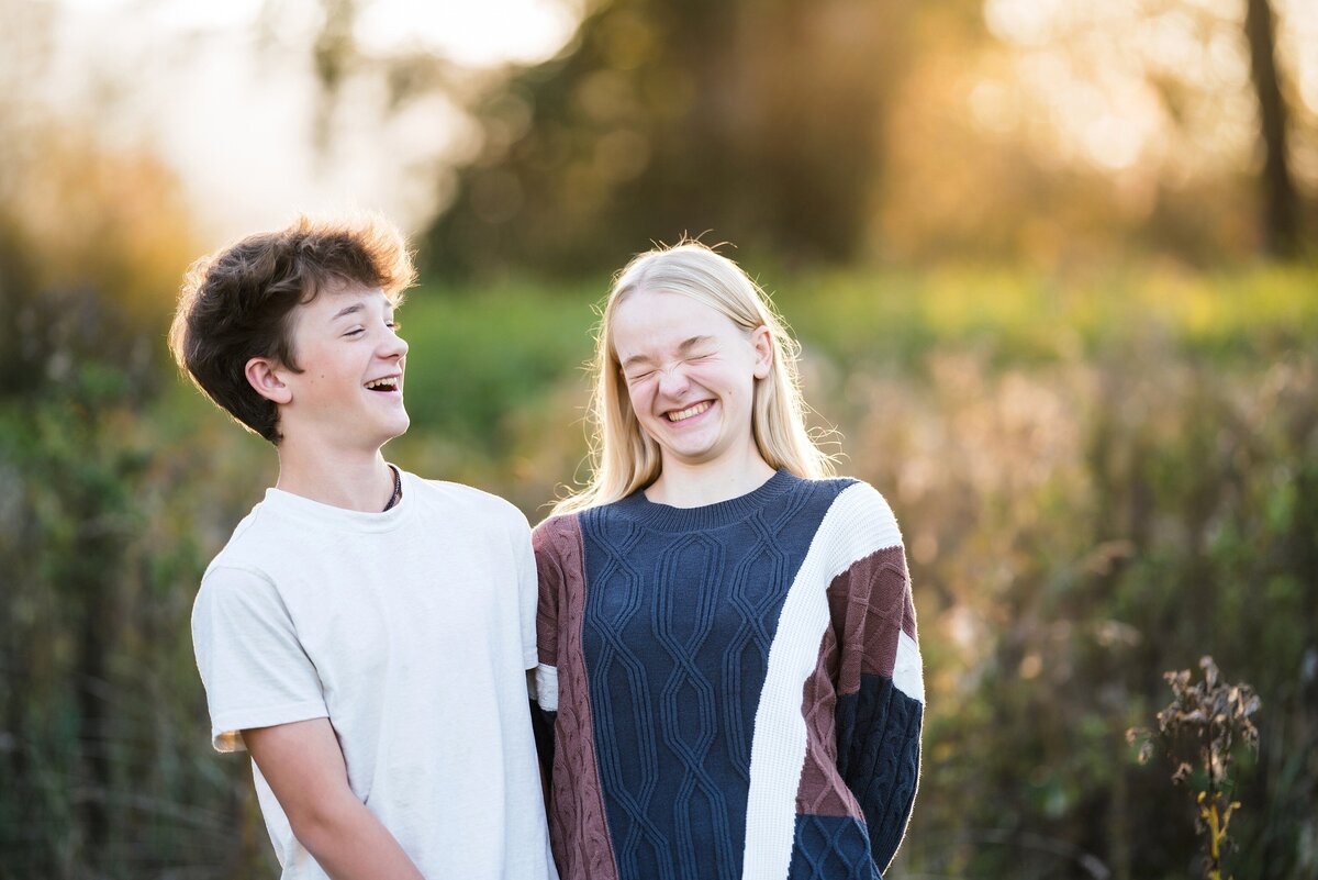 Teen brother and sister laughing together in a field at sunset