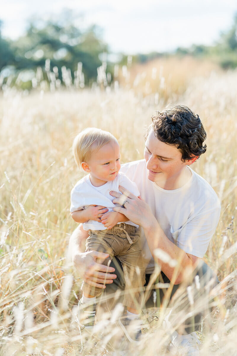 a father bends down to his toddler son and smiles at him for their Austin family photography session.