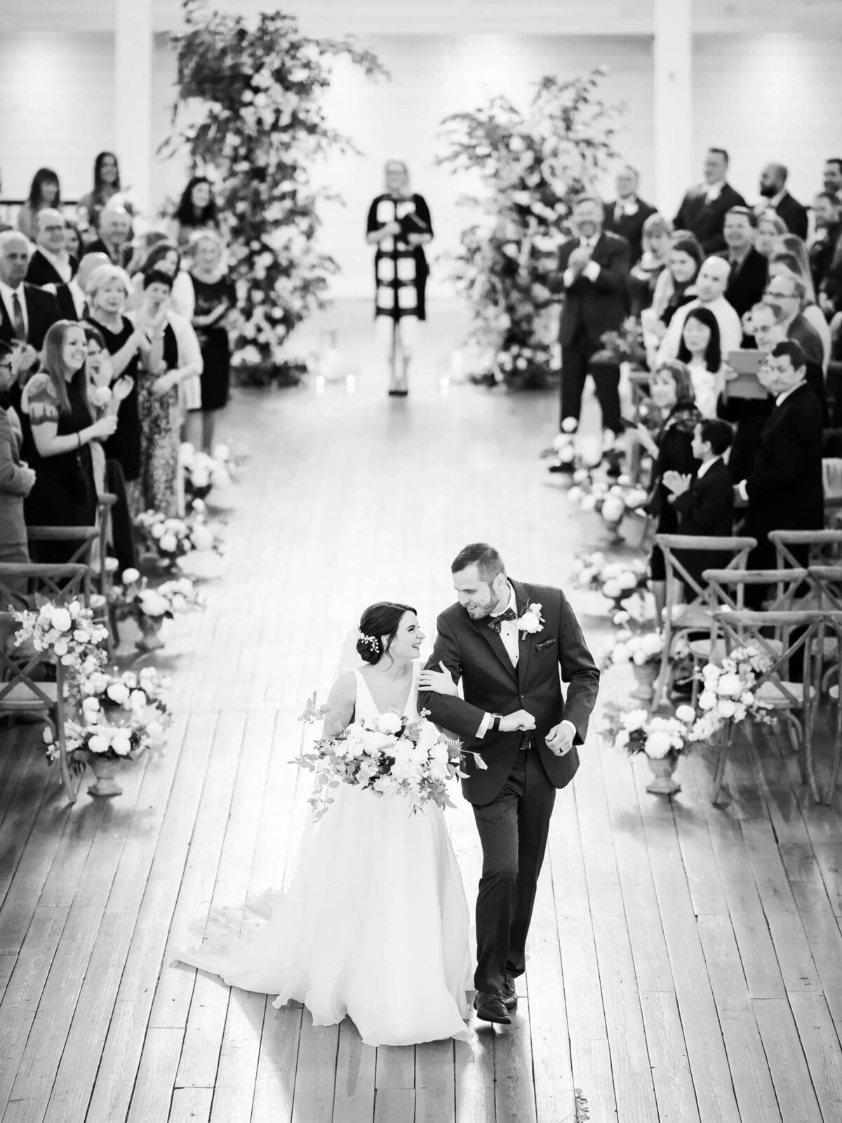 Bride and groom walking down the aisle post-ceremony, surrounded by guests and florals