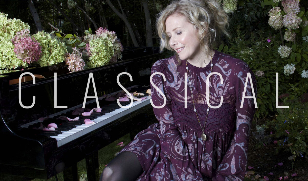 Classical musician photo Linda Brooks wearing purple dress sitting beside piano surrounded with flowers