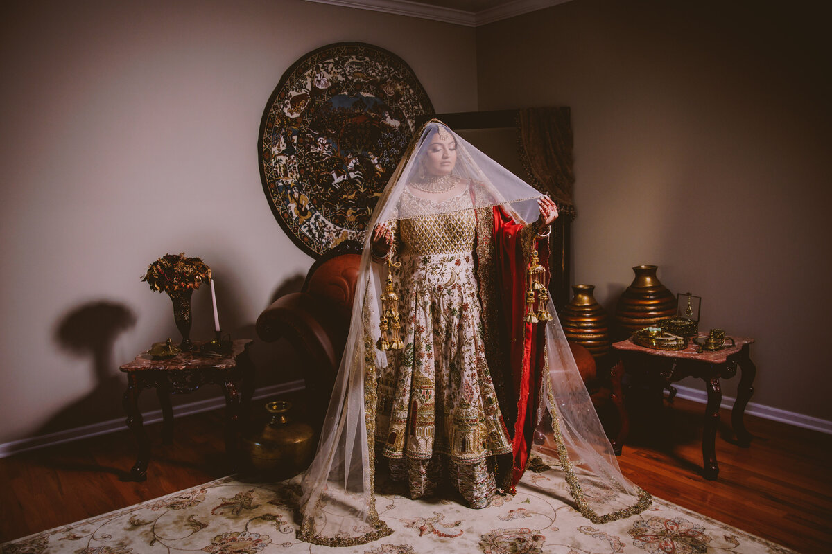 A sikh bride stands with the dupatta veil over her head during the getting ready bridal prep before the wedding