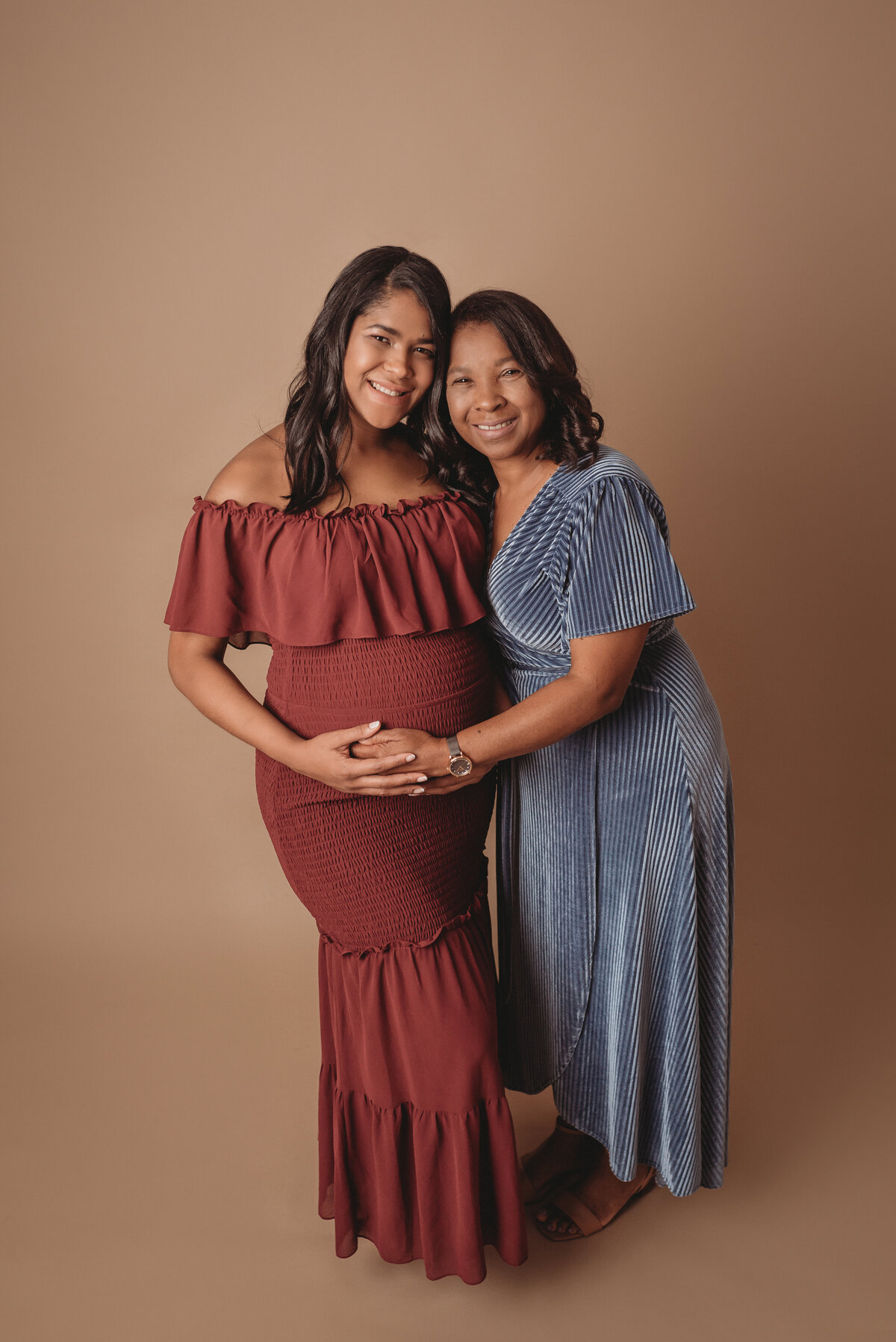 Pregnancy picture with mom to be and her mom. Mom to be is wearing a burgundy dress and her mom is wearing a blue velvet wrap dress.
