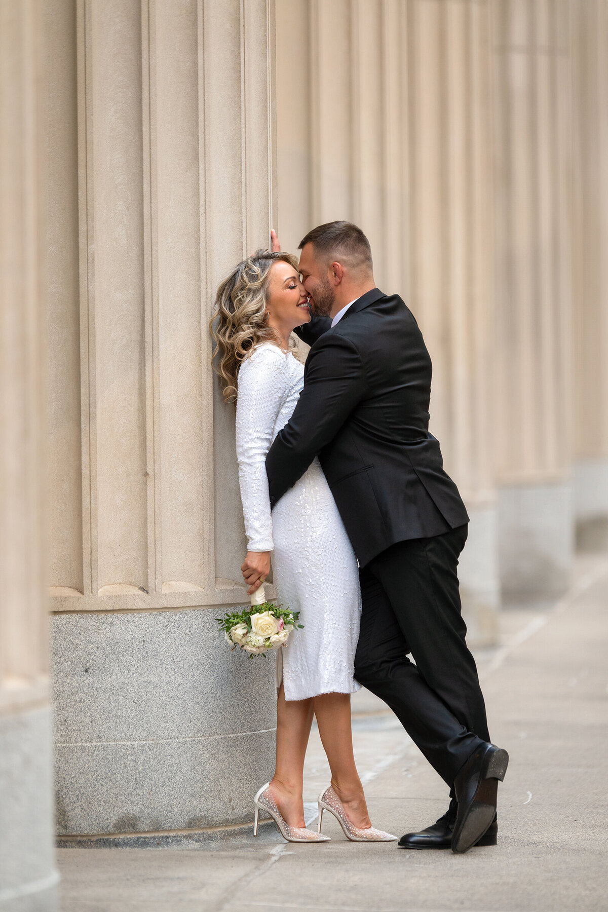 Groom is kissing her bride against the  columns of  Chicago buildig