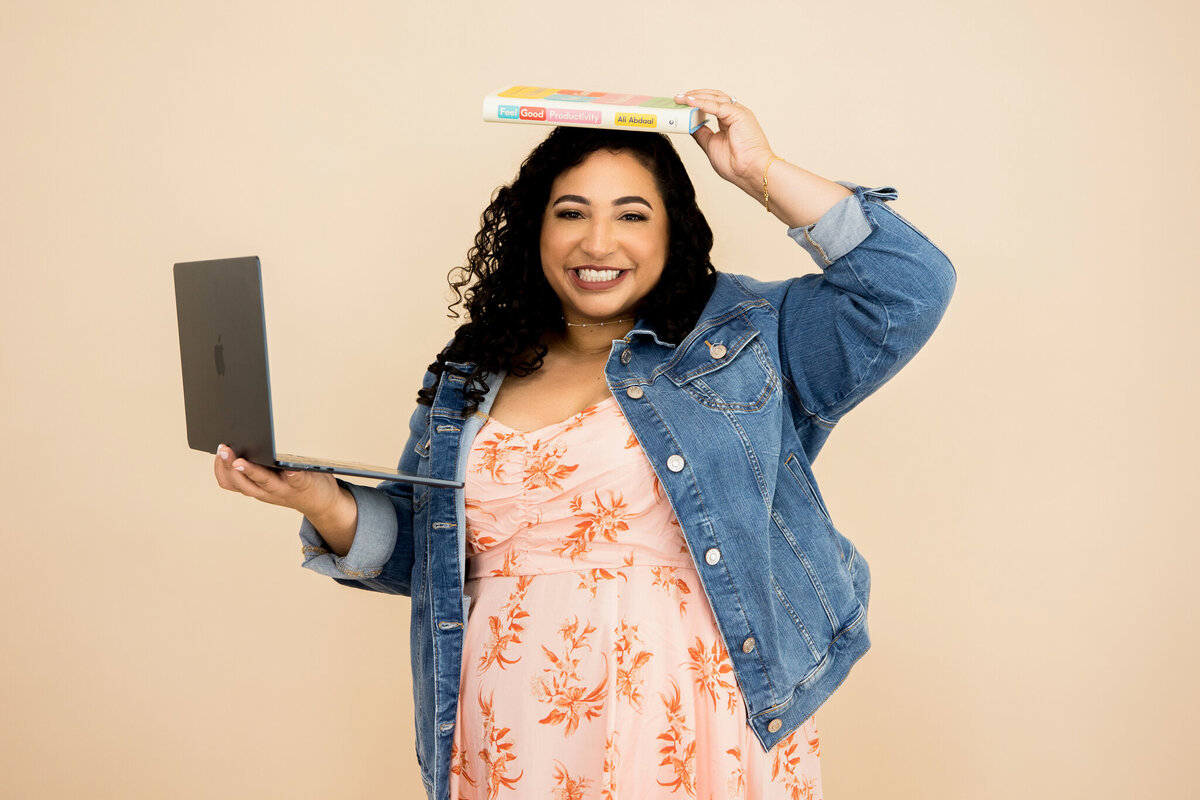 Heather balancing a laptop and book while smiling—great for brand photoshoot content on work-life balance and fun office moments.