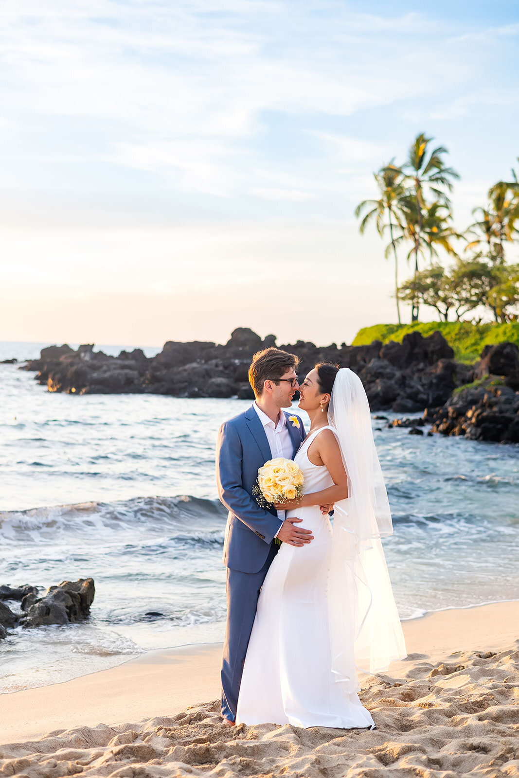 bride and groom kissing on the beach with veil,  white gown, and blue suit
