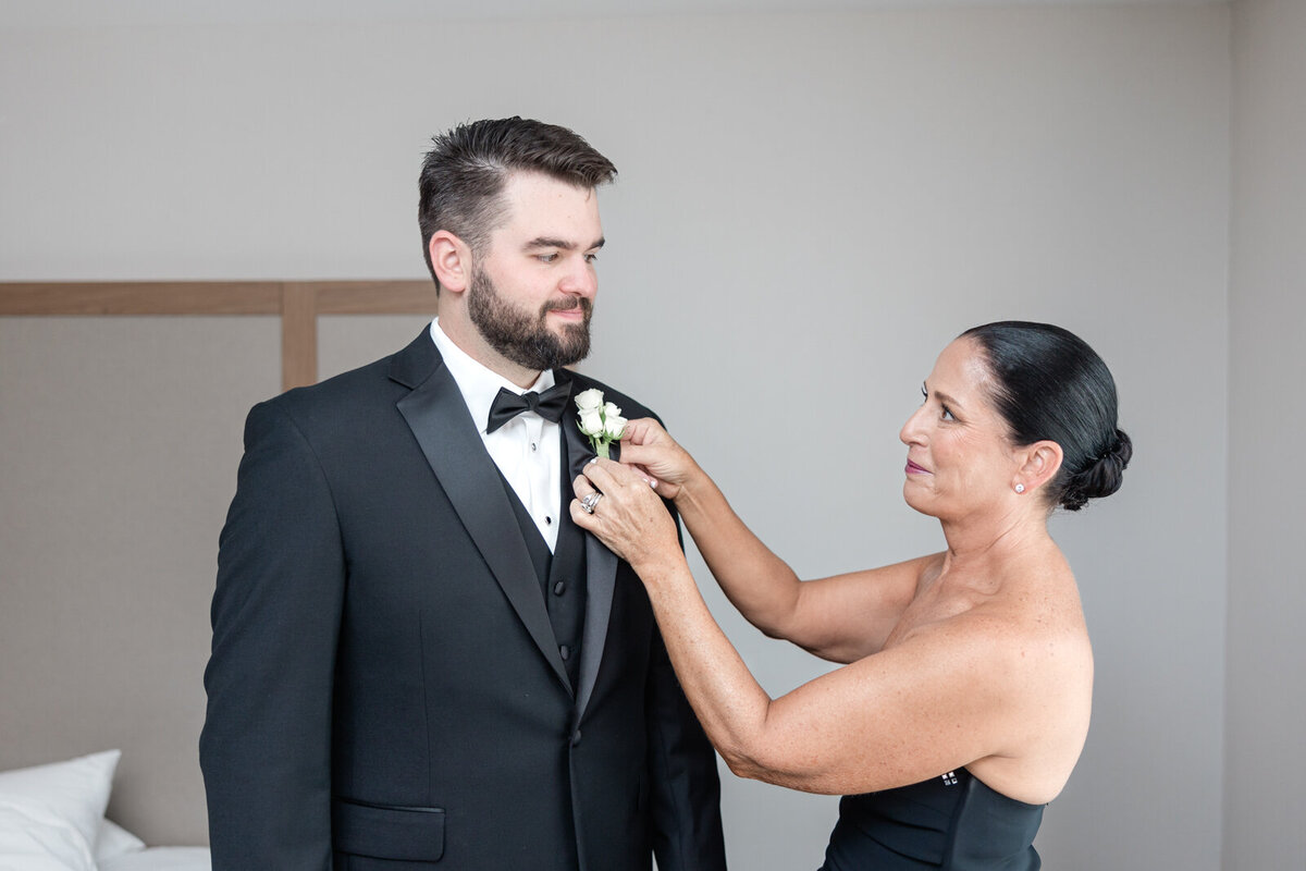 The mother of the groom pins a boutonniere on her son