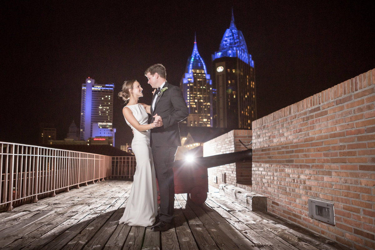 The bride and groom pose for a photo at Ft. Gaines with the city of Mobile, Alabama skyline in the background.