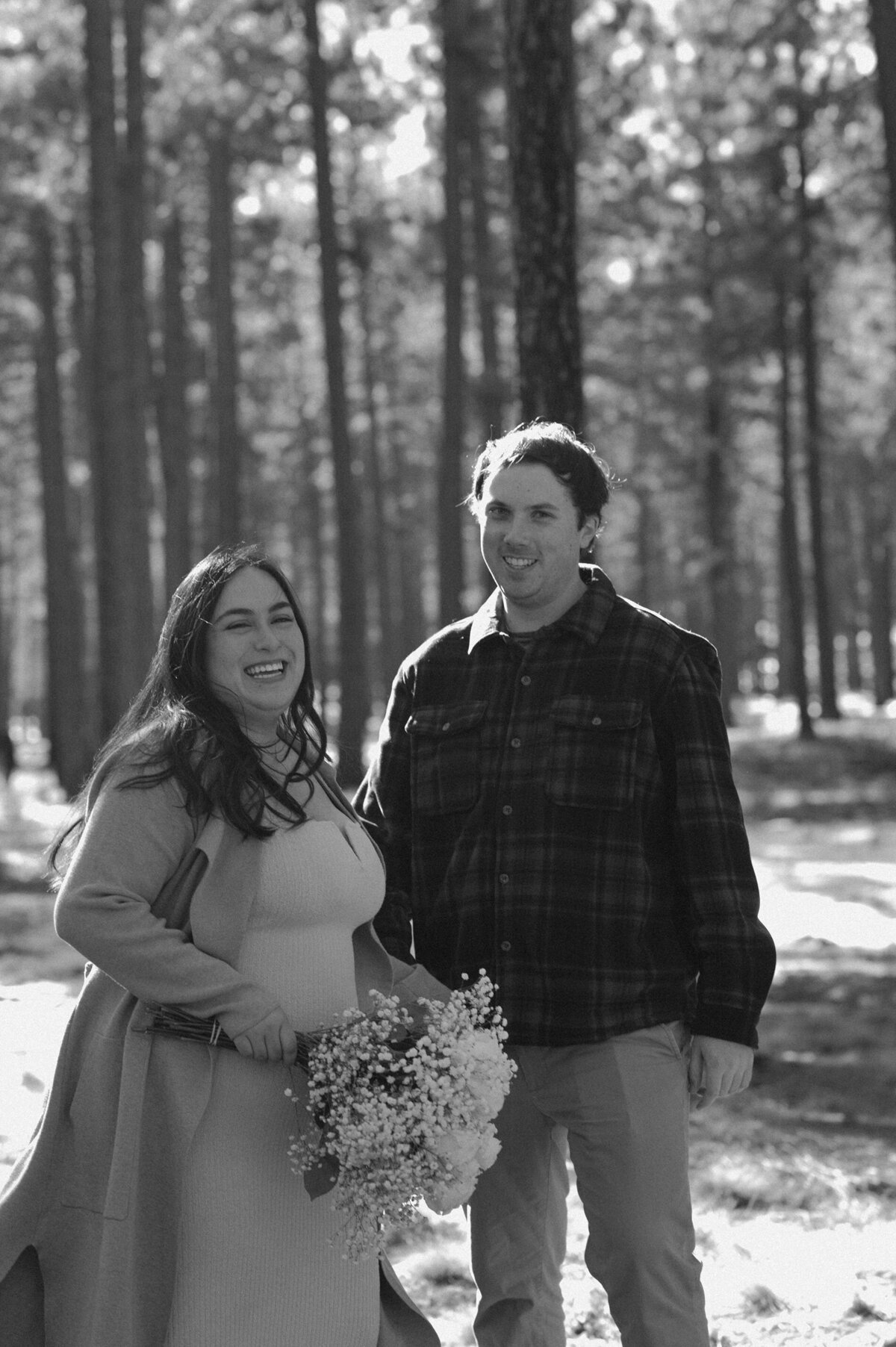 bride holding flowers and laughing as she stands next to her groom among the trees in Bend, Oregon