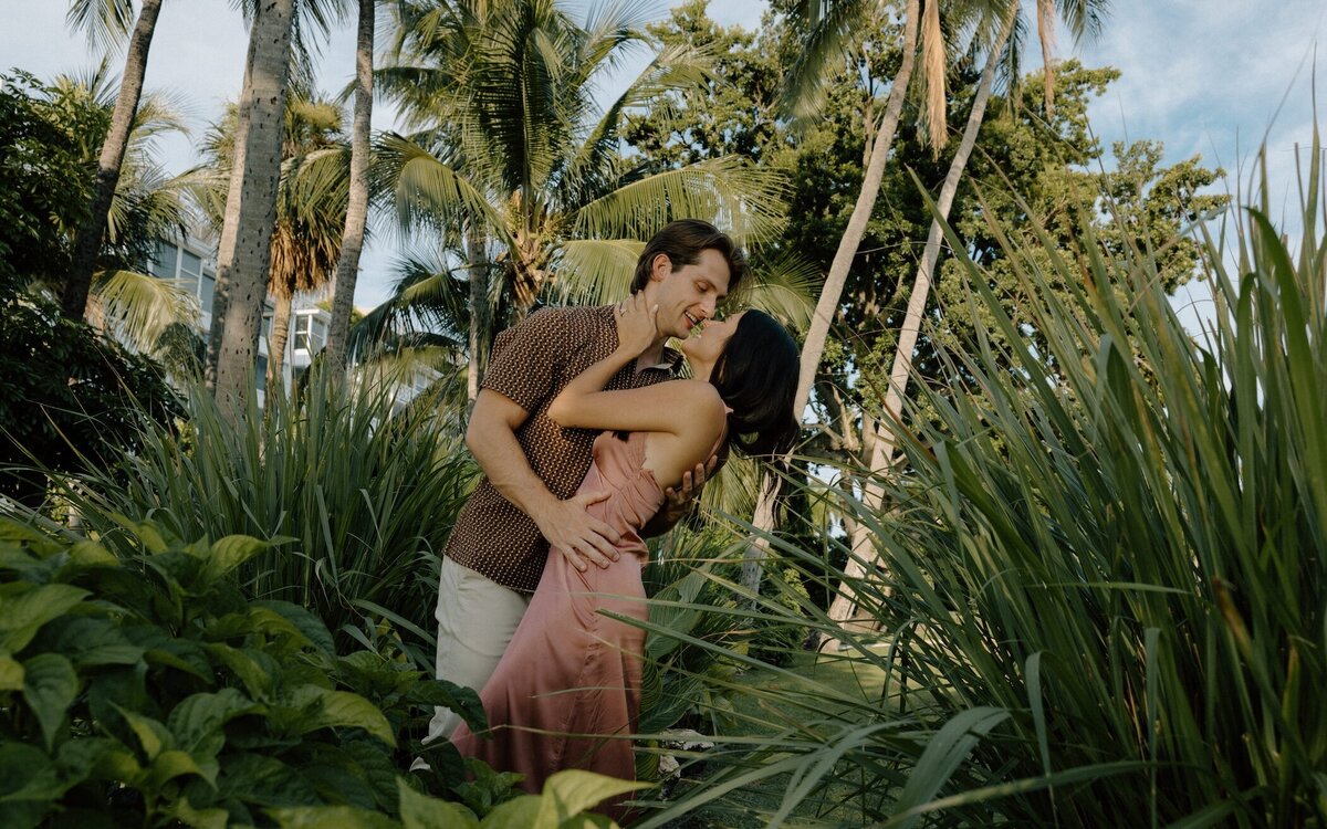 couple shares a kiss surrounded by palm trees and greenery